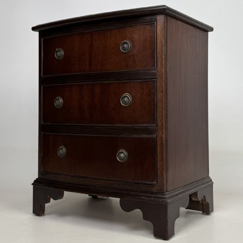 fig 1. A dark mahogany small chest of three drawers featuring brass ring pull handles and bracket feet.