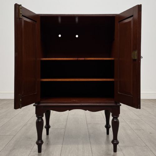 fig 1. A small dark mahogany cabinet featuring two panelled doors, a shaped apron, and four turned legs.