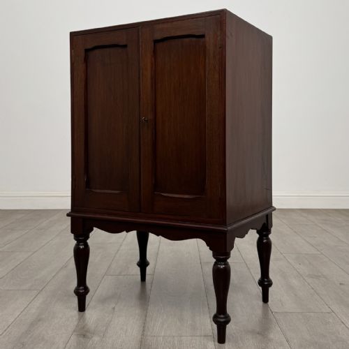 fig 2. A small dark mahogany cabinet featuring two panelled doors, a shaped apron, and four turned legs.