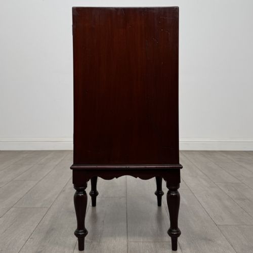 fig 3. A small dark mahogany cabinet featuring two panelled doors, a shaped apron, and four turned legs.