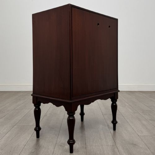 fig 4. A small dark mahogany cabinet featuring two panelled doors, a shaped apron, and four turned legs.