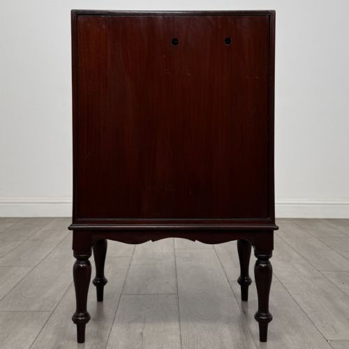 fig 5. A small dark mahogany cabinet featuring two panelled doors, a shaped apron, and four turned legs.