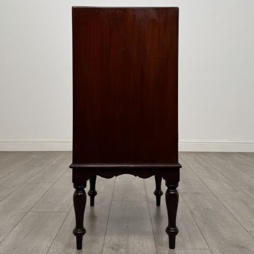 fig 7. A small dark mahogany cabinet featuring two panelled doors, a shaped apron, and four turned legs.