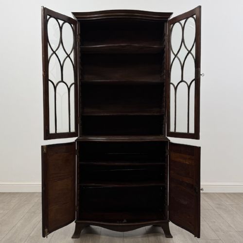 fig 1. A tall dark mahogany bookcase featuring a serpentine front profile, upper astragal glazed double doors, and a lower double-door cupboard.