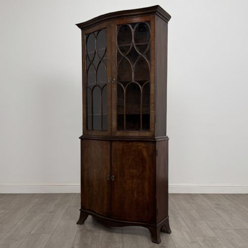fig 2. A tall dark mahogany bookcase featuring a serpentine front profile, upper astragal glazed double doors, and a lower double-door cupboard.