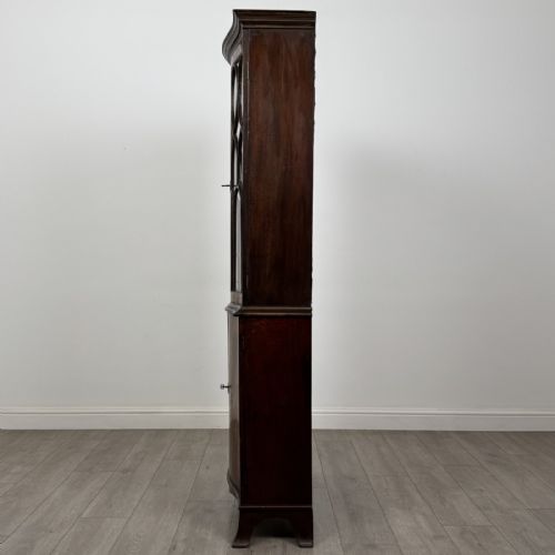 fig 3. A tall dark mahogany bookcase featuring a serpentine front profile, upper astragal glazed double doors, and a lower double-door cupboard.