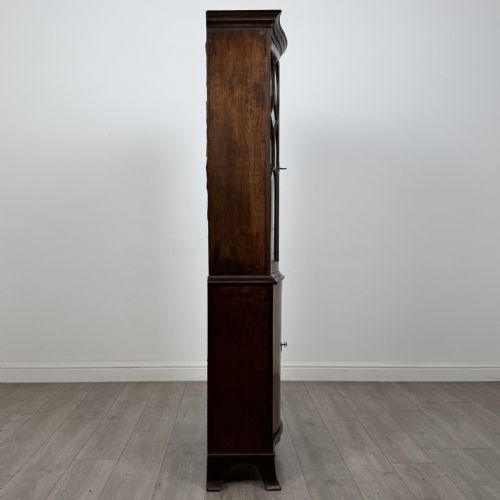fig 7. A tall dark mahogany bookcase featuring a serpentine front profile, upper astragal glazed double doors, and a lower double-door cupboard.