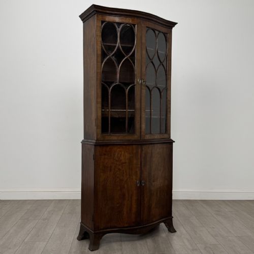 fig 8. A tall dark mahogany bookcase featuring a serpentine front profile, upper astragal glazed double doors, and a lower double-door cupboard.