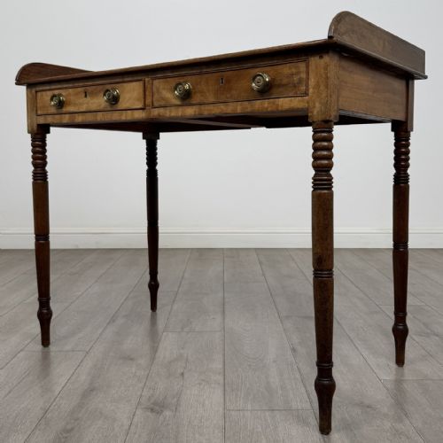 fig 1. An antique Georgian mahogany writing table featuring a raised gallery edge, two frieze drawers with brass circular handles, and slender turned legs.