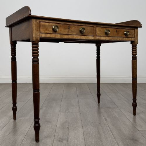 fig 7. An antique Georgian mahogany writing table featuring a raised gallery edge, two frieze drawers with brass circular handles, and slender turned legs.