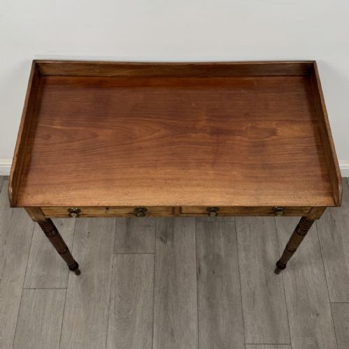 fig 8. An antique Georgian mahogany writing table featuring a raised gallery edge, two frieze drawers with brass circular handles, and slender turned legs.