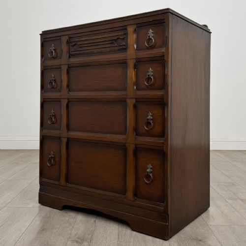 fig 1. A dark brown oak chest of drawers with geometric panel moulding, four horizontal drawers, ornate metal ring handles, and a plinth base.