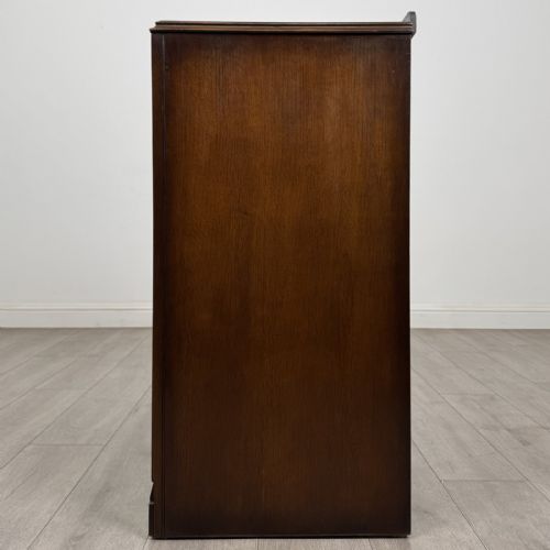 fig 2. A dark brown oak chest of drawers with geometric panel moulding, four horizontal drawers, ornate metal ring handles, and a plinth base.