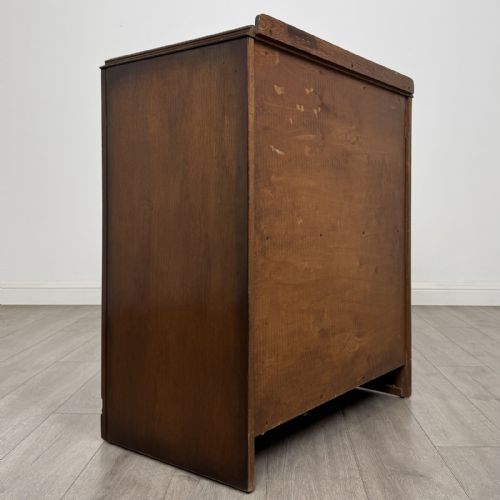 fig 3. A dark brown oak chest of drawers with geometric panel moulding, four horizontal drawers, ornate metal ring handles, and a plinth base.