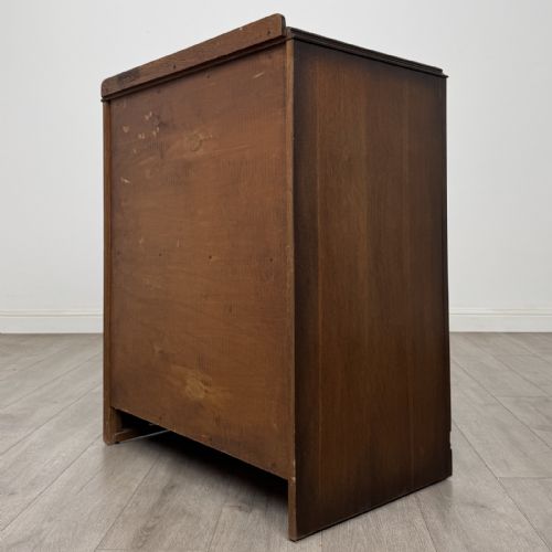 fig 5. A dark brown oak chest of drawers with geometric panel moulding, four horizontal drawers, ornate metal ring handles, and a plinth base.