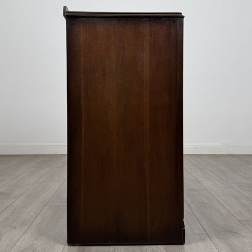 fig 6. A dark brown oak chest of drawers with geometric panel moulding, four horizontal drawers, ornate metal ring handles, and a plinth base.
