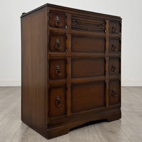 fig 7. A dark brown oak chest of drawers with geometric panel moulding, four horizontal drawers, ornate metal ring handles, and a plinth base.