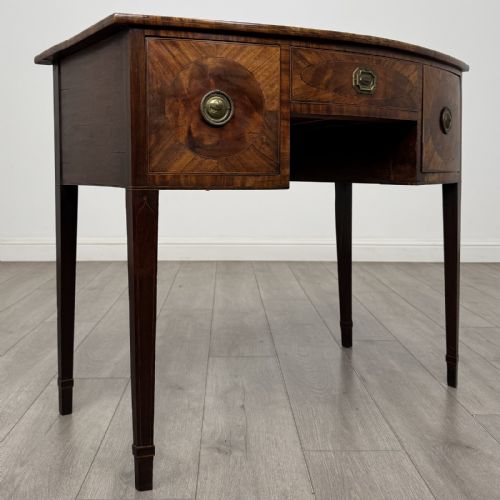 fig 7. An antique Georgian mahogany bow-front side table with flame mahogany inlaid drawers, brass ring handles, and tapered square legs.