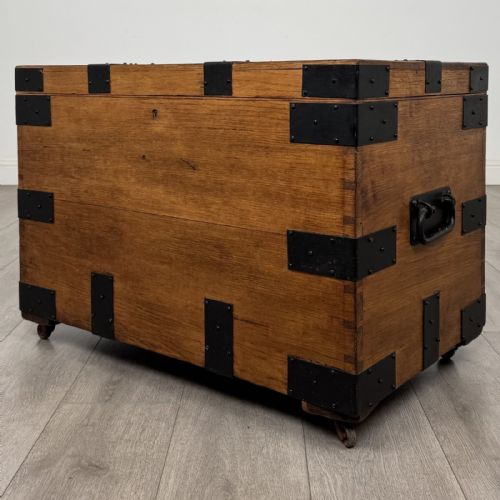 fig 1. A rectangular warm brown oak storage chest featuring black metal strap reinforcement, a keyhole, and corner brackets on small castors.