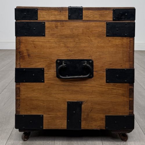 fig 2. A rectangular warm brown oak storage chest featuring black metal strap reinforcement, a keyhole, and corner brackets on small castors.