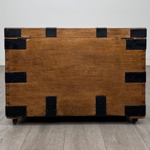 fig 4. A rectangular warm brown oak storage chest featuring black metal strap reinforcement, a keyhole, and corner brackets on small castors.