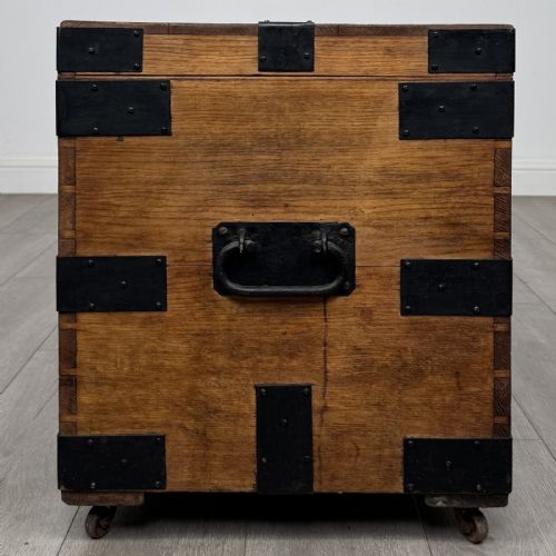 fig 6. A rectangular warm brown oak storage chest featuring black metal strap reinforcement, a keyhole, and corner brackets on small castors.
