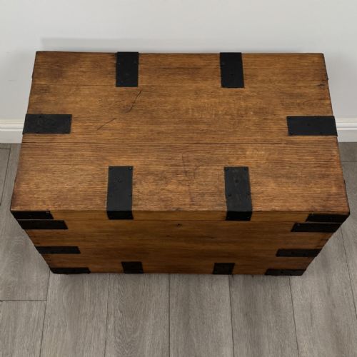 fig 8. A rectangular warm brown oak storage chest featuring black metal strap reinforcement, a keyhole, and corner brackets on small castors.
