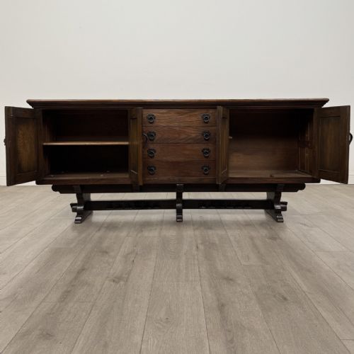fig 1. A large dark carved oak sideboard featuring panelled cupboard doors with iron strap hinges, central drawers, and a carved low stretcher base.