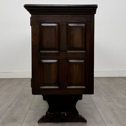 fig 3. A large dark carved oak sideboard featuring panelled cupboard doors with iron strap hinges, central drawers, and a carved low stretcher base.
