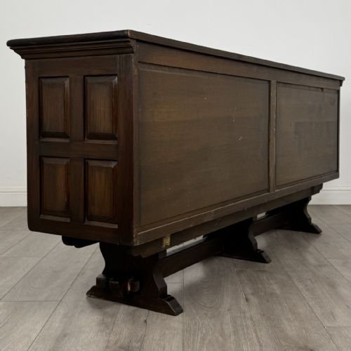 fig 4. A large dark carved oak sideboard featuring panelled cupboard doors with iron strap hinges, central drawers, and a carved low stretcher base.