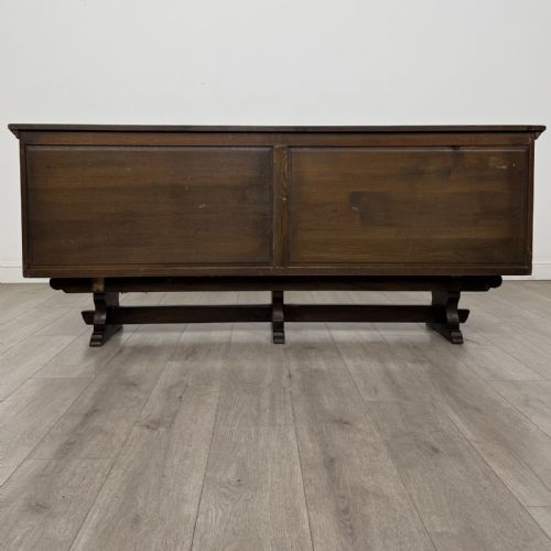 fig 5. A large dark carved oak sideboard featuring panelled cupboard doors with iron strap hinges, central drawers, and a carved low stretcher base.