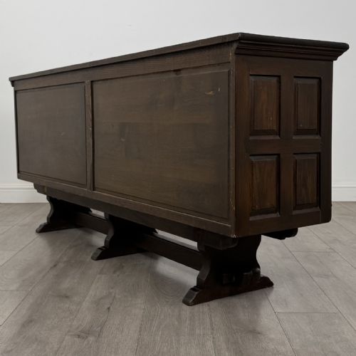 fig 6. A large dark carved oak sideboard featuring panelled cupboard doors with iron strap hinges, central drawers, and a carved low stretcher base.