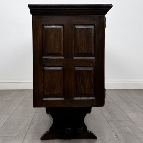 fig 7. A large dark carved oak sideboard featuring panelled cupboard doors with iron strap hinges, central drawers, and a carved low stretcher base.