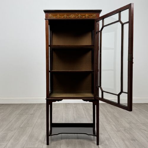 fig 1. An Edwardian mahogany display cabinet featuring a painted inlaid floral frieze, single astragal glazed door, fabric-lined interior shelves, and tapered legs with a lower undertier.