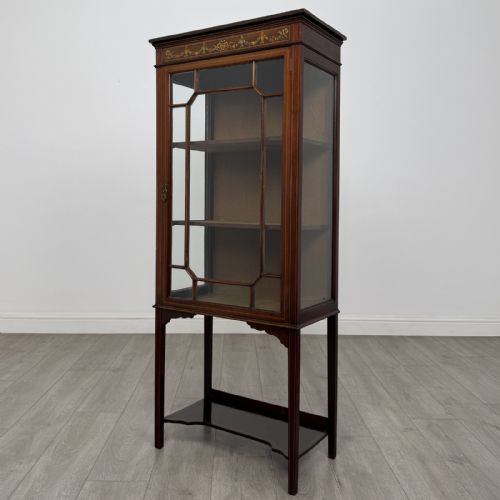 fig 2. An Edwardian mahogany display cabinet featuring a painted inlaid floral frieze, single astragal glazed door, fabric-lined interior shelves, and tapered legs with a lower undertier.