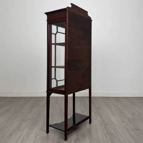 fig 4. An Edwardian mahogany display cabinet featuring a painted inlaid floral frieze, single astragal glazed door, fabric-lined interior shelves, and tapered legs with a lower undertier.