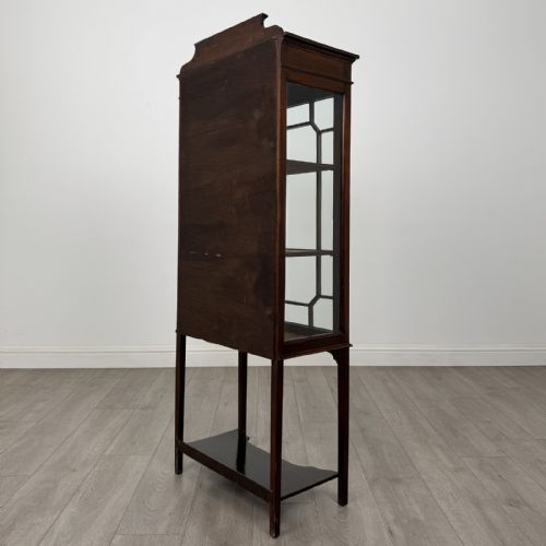 fig 6. An Edwardian mahogany display cabinet featuring a painted inlaid floral frieze, single astragal glazed door, fabric-lined interior shelves, and tapered legs with a lower undertier.