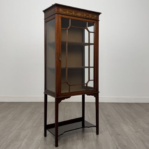 fig 8. An Edwardian mahogany display cabinet featuring a painted inlaid floral frieze, single astragal glazed door, fabric-lined interior shelves, and tapered legs with a lower undertier.