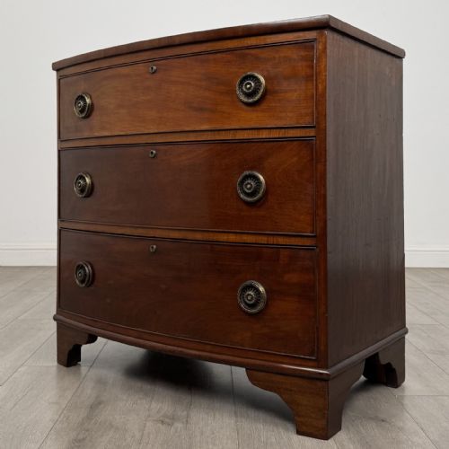 fig 1. A Georgian mahogany bow front chest of drawers featuring three horizontal drawers with brass ring handles and bracket feet.