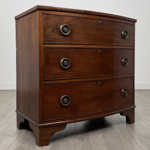 fig 7. A Georgian mahogany bow front chest of drawers featuring three horizontal drawers with brass ring handles and bracket feet.