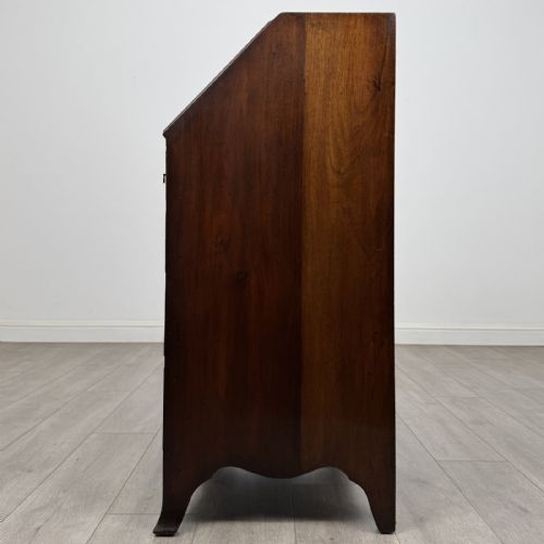 fig 1. A small Georgian style dark mahogany writing bureau featuring an inlaid oval motif on the slant-front lid and four drawers with brass handles.