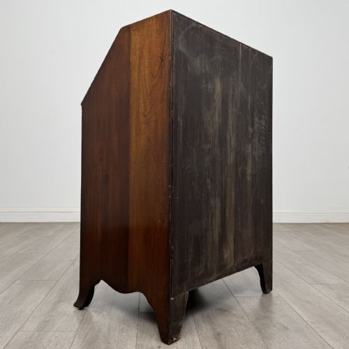 fig 2. A small Georgian style dark mahogany writing bureau featuring an inlaid oval motif on the slant-front lid and four drawers with brass handles.
