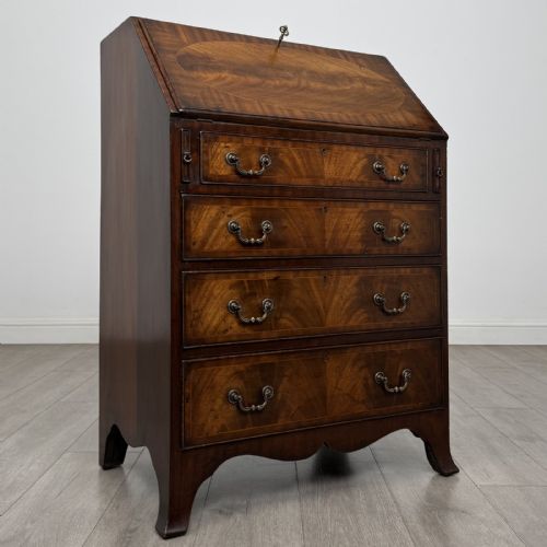 fig 6. A small Georgian style dark mahogany writing bureau featuring an inlaid oval motif on the slant-front lid and four drawers with brass handles.