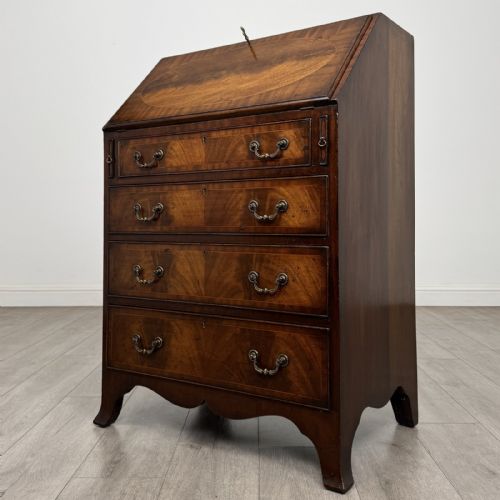 fig 7. A small Georgian style dark mahogany writing bureau featuring an inlaid oval motif on the slant-front lid and four drawers with brass handles.