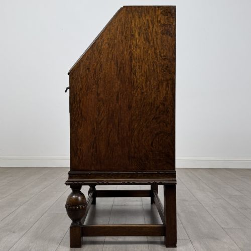 fig 3. An antique dark oak fall-front writing bureau featuring a carved oval motif on the sloping lid, two lower drawers with wooden handles, and bulbous turned front legs on a stretcher base.