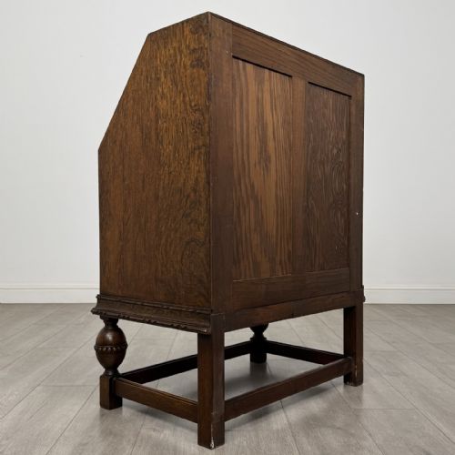 fig 4. An antique dark oak fall-front writing bureau featuring a carved oval motif on the sloping lid, two lower drawers with wooden handles, and bulbous turned front legs on a stretcher base.