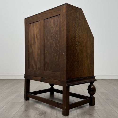 fig 6. An antique dark oak fall-front writing bureau featuring a carved oval motif on the sloping lid, two lower drawers with wooden handles, and bulbous turned front legs on a stretcher base.