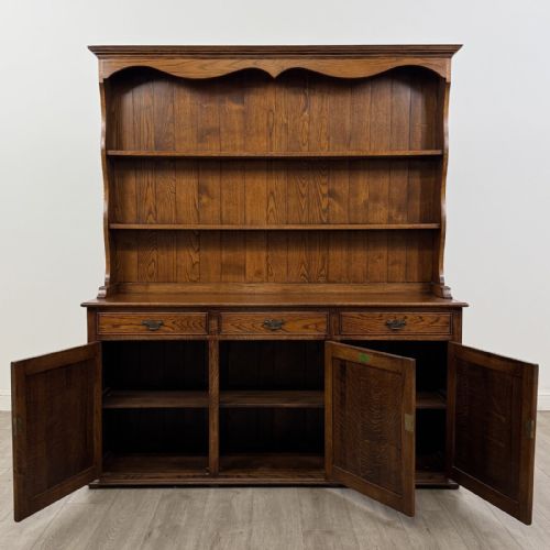 fig 1. A vintage dark oak Welsh dresser featuring an upper open shelving rack with a shaped top apron and a lower storage unit with three drawers and three panelled cupboard doors.
