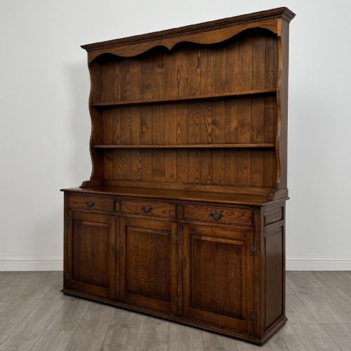 fig 2. A vintage dark oak Welsh dresser featuring an upper open shelving rack with a shaped top apron and a lower storage unit with three drawers and three panelled cupboard doors.
