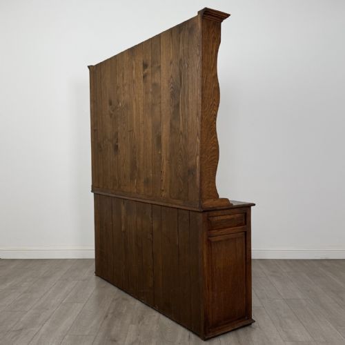fig 6. A vintage dark oak Welsh dresser featuring an upper open shelving rack with a shaped top apron and a lower storage unit with three drawers and three panelled cupboard doors.